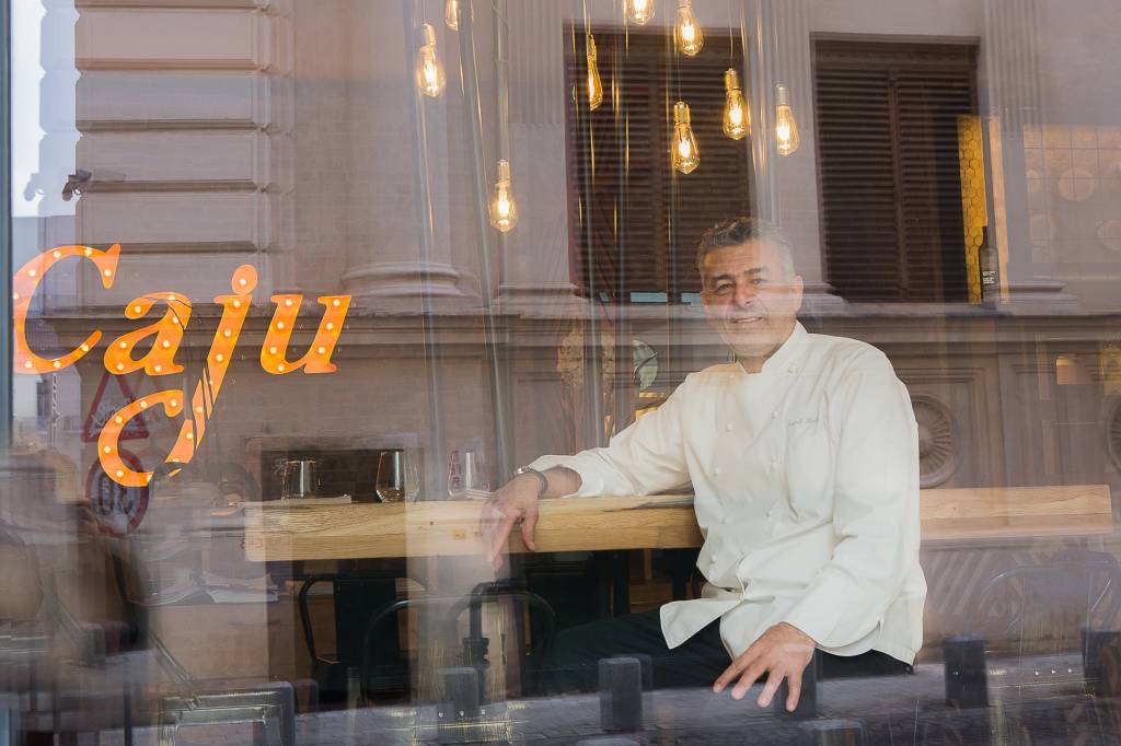Chef Hadad fotografiat din afara in braseria Caju by Joseph Hadad , in dreptul vitrinei, iar in fundal sigla braseriei luminatain dreptul vitrinei