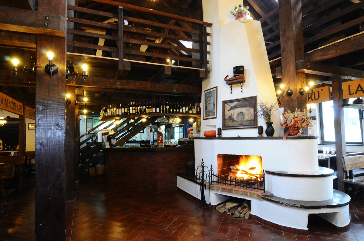 Taverna Sârbului Sinaia, cu semineu alb in prim plan si o scara din lemn care urca la etaj in fundal, unul din cele mai bune restaurante din Sinaia