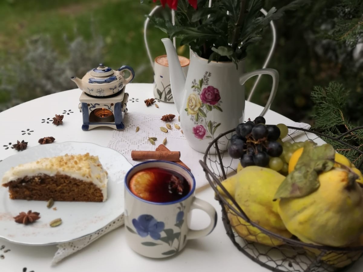 masa alba rotunda e care sunt asezate o cana cu ceai cald, o farfurie cu placinta, o vaza cu flori si un cos cu gutui, la ceainăria GreenTea