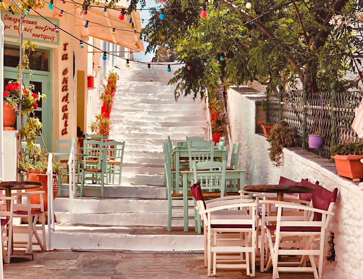 taverna din Grecia cu mese colorate asezate pe niste trepte albe si copaci in jur