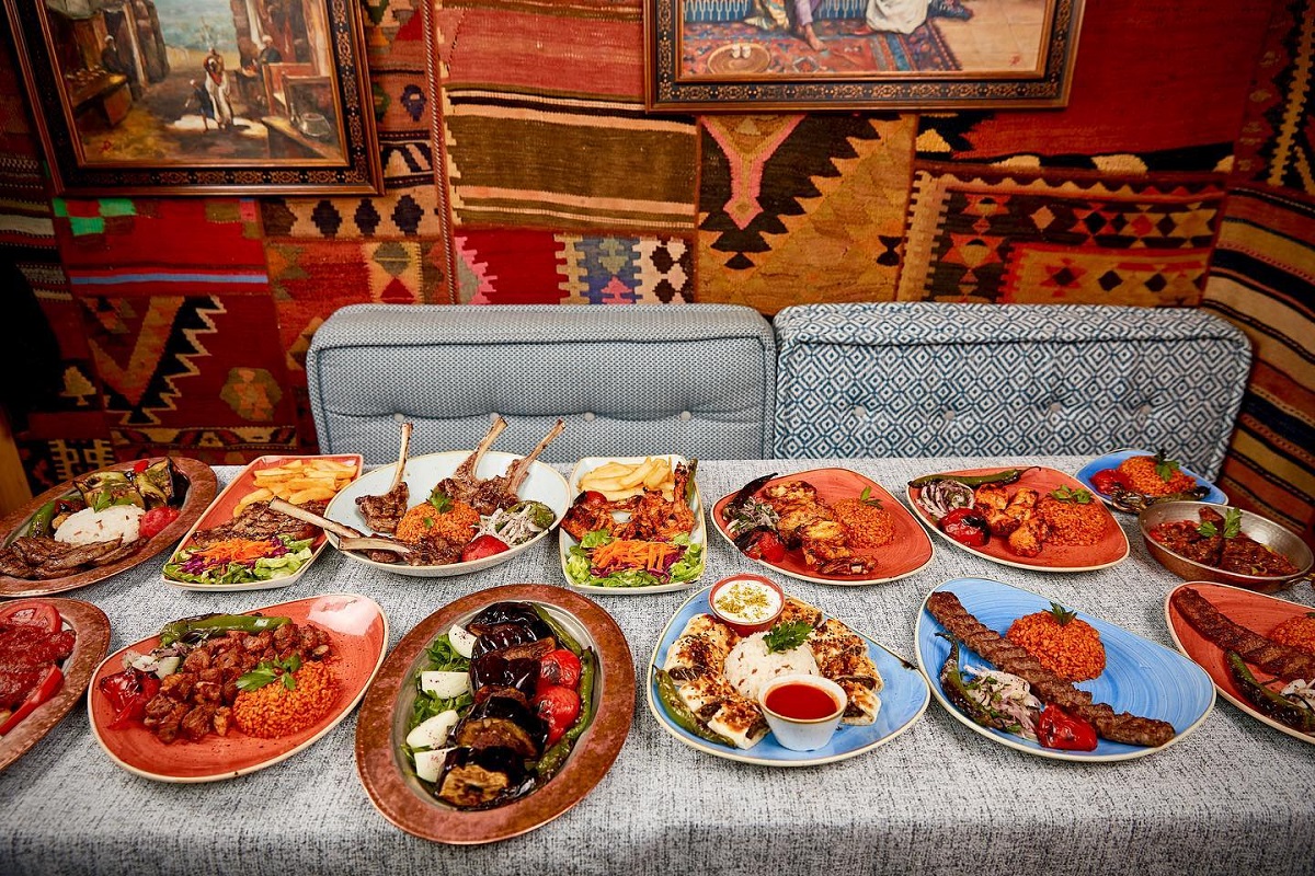masa intinsa plina cu farfurii cu multe preparate turcesti, in fata unei canapele gri, iar pe perete covoare turcesti, la restaurant divan din floreasca