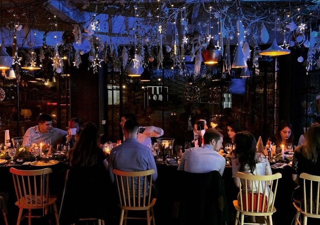 oameni asezati la o masa lunga, imbracati elegant, iar deasupra mesei un aranjament floral luminat in albastru, la Il Locale, un restaurant la care să ieși cu colegii la final de an, de Crăciun