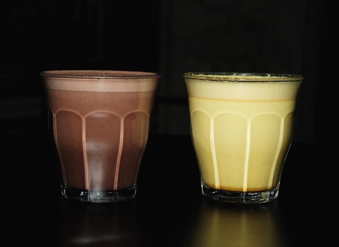 2 pahare fotografiate pe fundal negru, unul cu hot choco, altul cu golden milk de la Artichoke Social House București