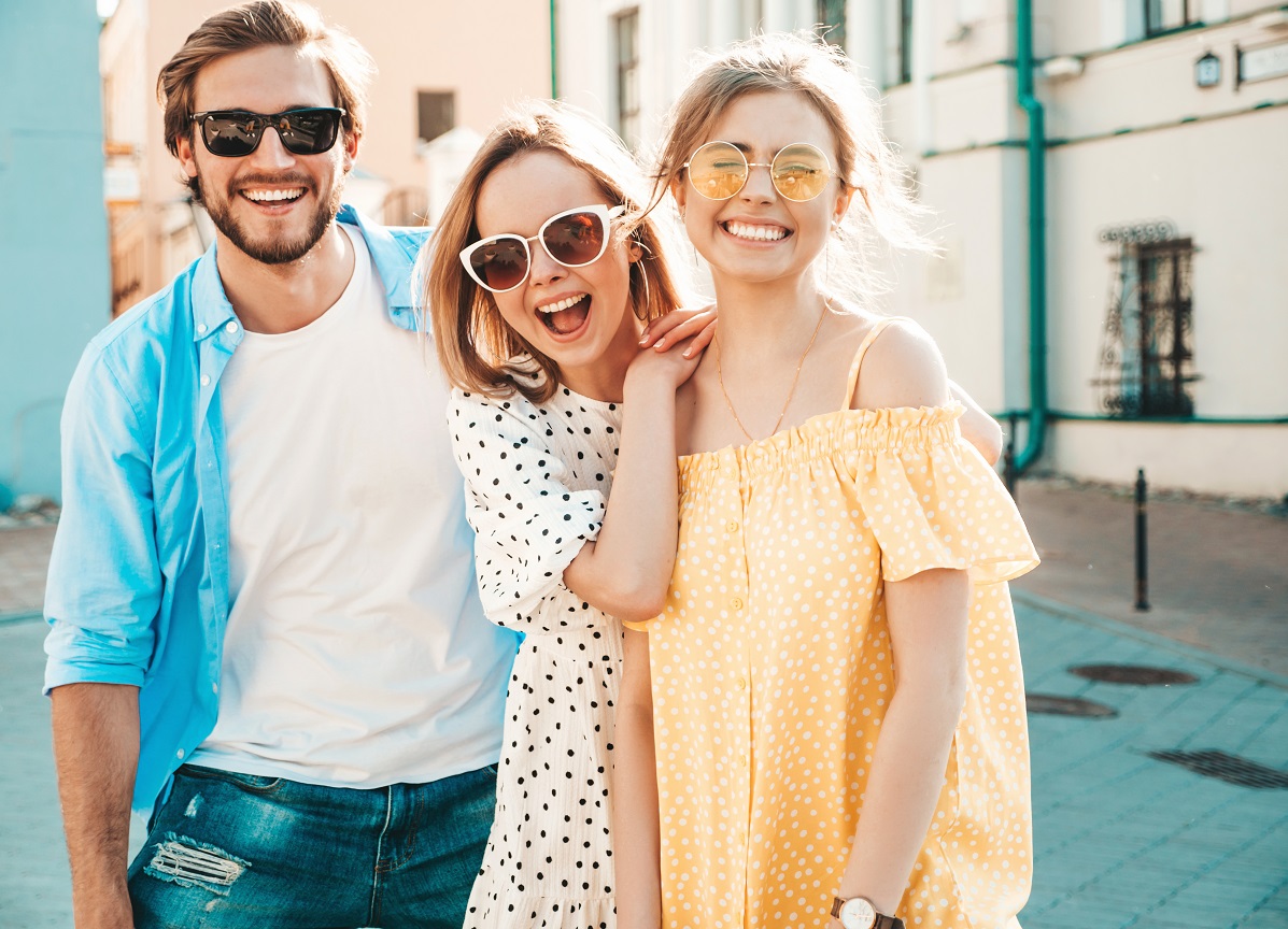 Grup de prieteni, un baiat si doua fete, imbracati in haine de vara, cu ochelari de soare, care sugereaza o iesire in oras in weekend