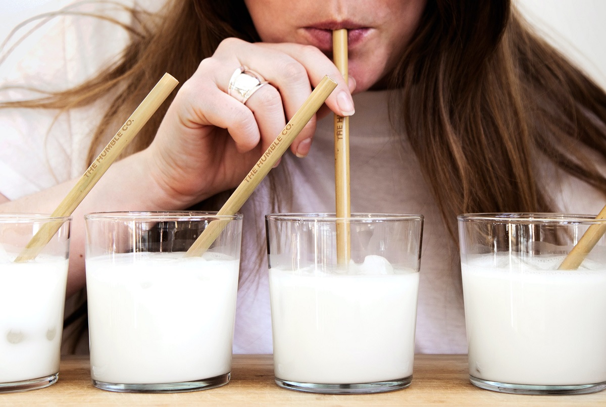 closeup cu o femeie cu par lung care soarbe cu paiul dintr-un pahar cu lapte bun și sănătos, așezat lângă alte trei pahare de lapte identice