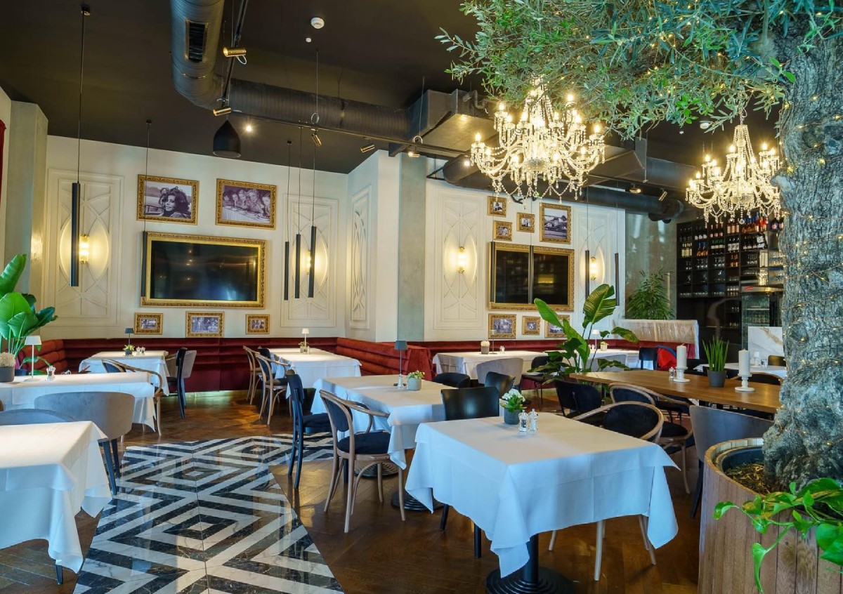 imagine din restaurantul Olivetto by Caelia, cu mese cu fete de masa albe, tablouri pe pereti, candelabre mari si ghivece cu flori inalte, unul din restaurante noi București 2021