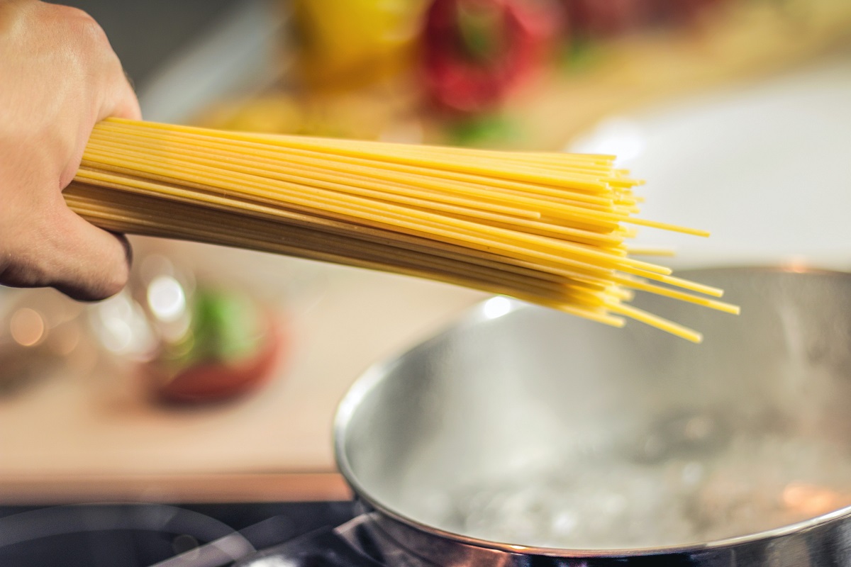 o mana de spaghete deasupra unei oale cu apa care fierbe, urmand a fi gatite