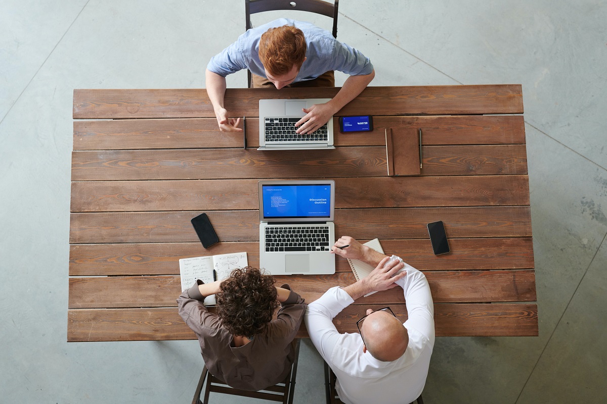 oameni de afaceri fotografiati de sus, la birou, cu laptop in fata, imagine sugestiva pentru ghid de renegociere