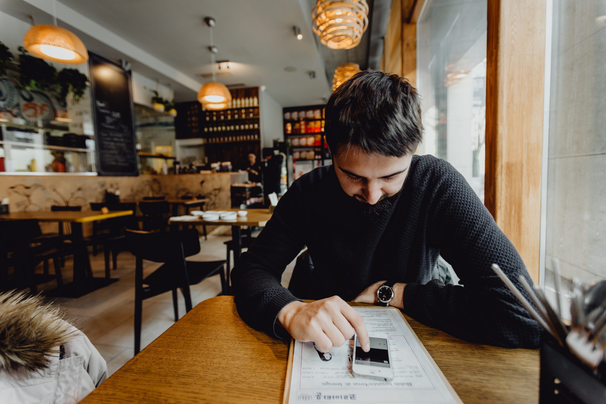barbat stand la masa in restaurant gol, cu capul plecat, uitandu-se in telefom, imagine reprezentativa pentru restaurantele afectate de coronavirus