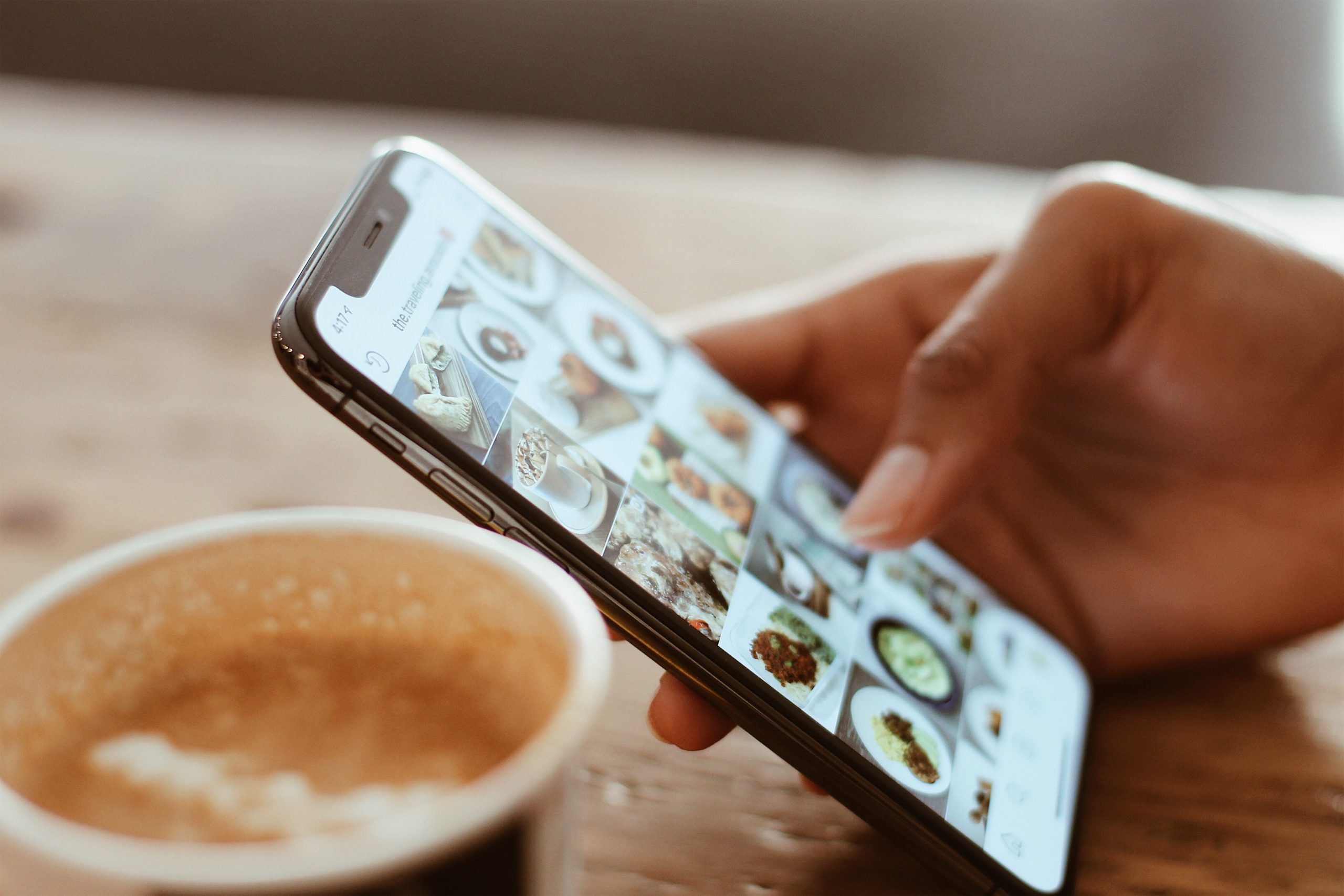 focus pe un telefon tinut in mana, cu cineva care navigheaza poze, imagine sugestiva pentru restaurante de la care poți comanda mâncare acasă