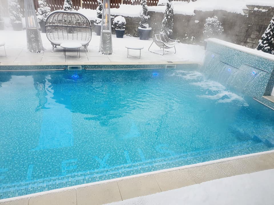 piscina exterioara incalzita, fotografiata iarna, cu mobilier de pe margine plin de zapada