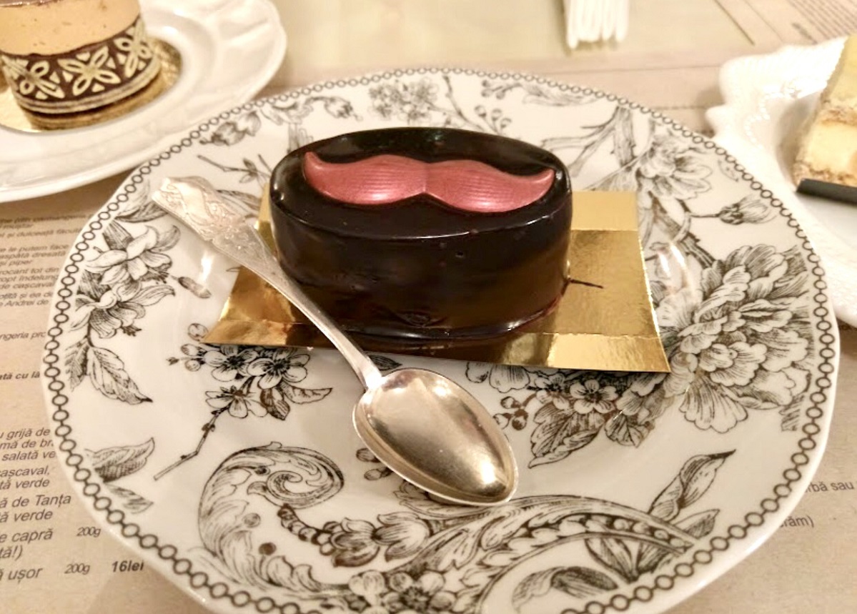 prajitura de ciocolata decorata cu crema de zmeura, in forma de mustata, asezata pe o farfurie retro, cu o lingurita, la Zexe Braserie