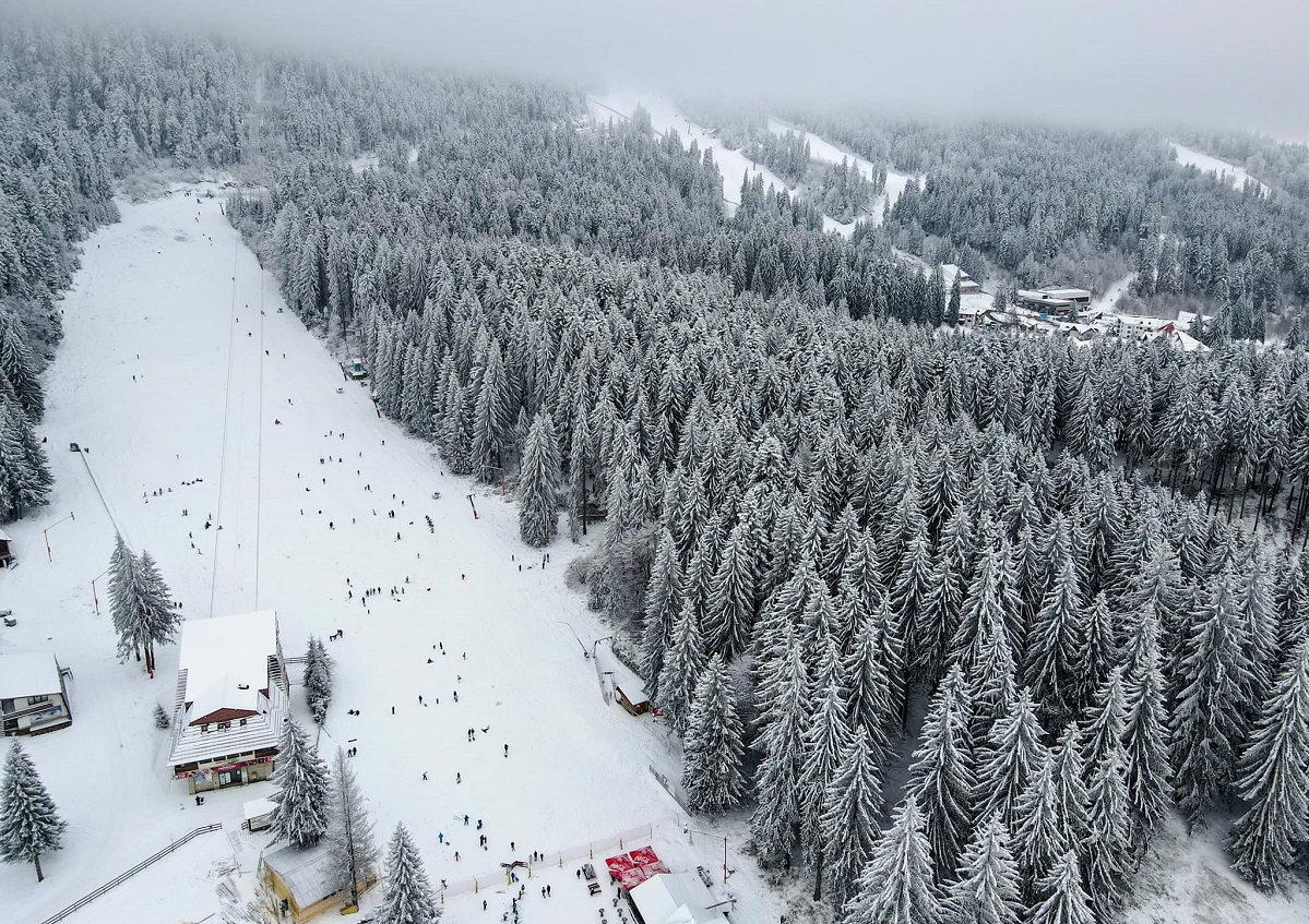 vedere de sus asupra partiei principale din Poaiana Brașov, cu oameni care schiază, si brazii plini de zăpada, stațiune unde să faci Revelionul la munte