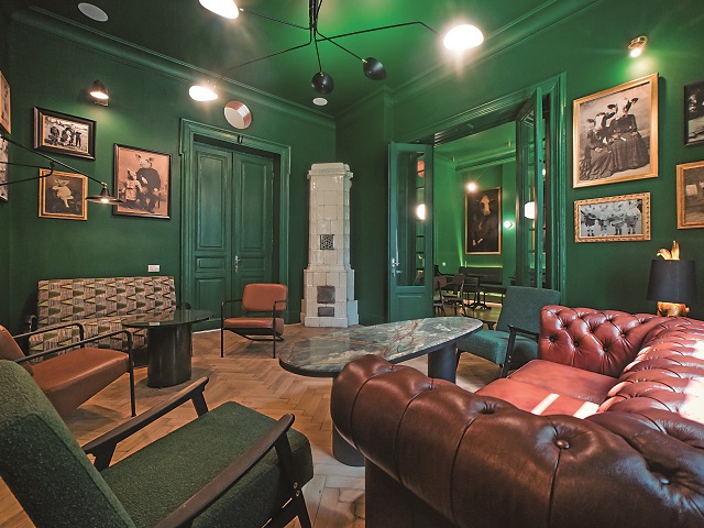 incapere cu pereti verde inchis, cu tablouri, o canapea masiva din piele, 2 fotolii si o soba, la Animaletto House București, unde să ieși cu prietenele de 1 martie