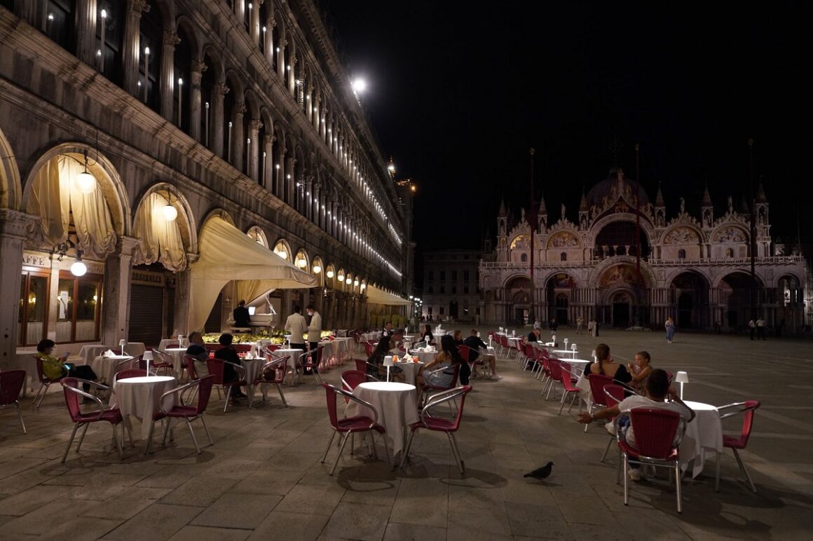 Restaurantul Qaudri din Piata St. Marco din Veneția, fotografiat seara, cu mese afara, in piata, la care iau masa clientii